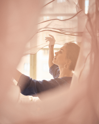 藝術家與漂浮的粉色綢緞布料共舞，象徵芍藥綻放時的柔美姿態與西西里蜜橘精油帶來的閃耀光影。