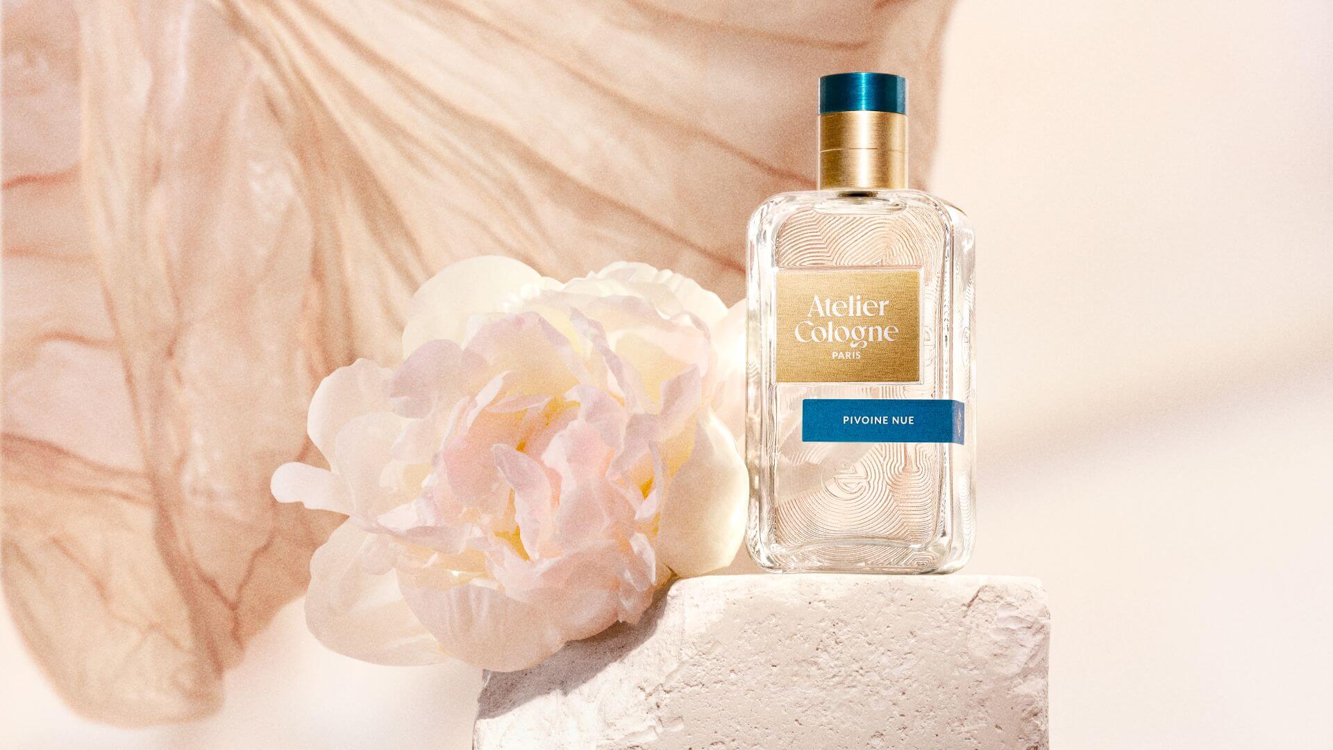 Atelier Cologne 無欲裸芍淡香精 Pivoine Nue 置於米白基座，環繞粉色輕盈綢緞與芍藥花卉，展現精醇系列香水的優雅藝術感。