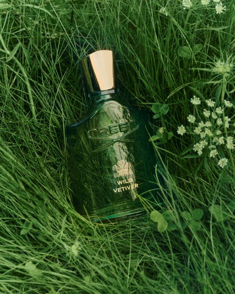 CREED Wild Vetiver 岩蘭野境香水瓶置於綠色草地間，自然清新木質花香意象